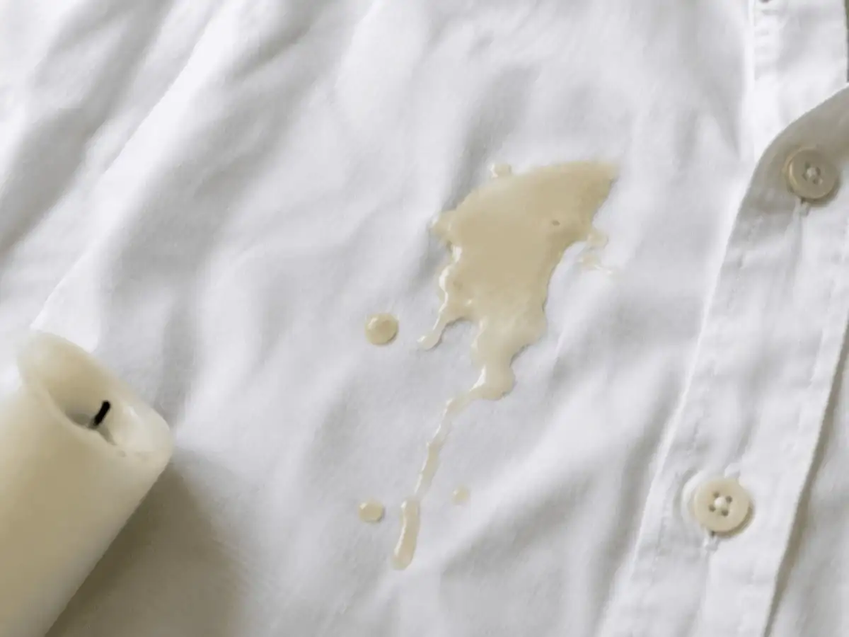 Candle wax can be easier to remove when hardened; freeze it first, then use a warm iron and paper towels to lift residue from fabric 