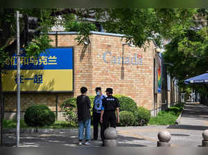 Police and security staff stand on a street next to the embassy of Canada where an Ukrainian flag with messages of support for Ukraine is seen on a wall, in Beijing on May 17, 2023. Authorities in China's capital have asked several embassies to remove political signs from their outer walls, multiple diplomatic sources told AFP. (Photo by Hector RETAMAL / AFP)