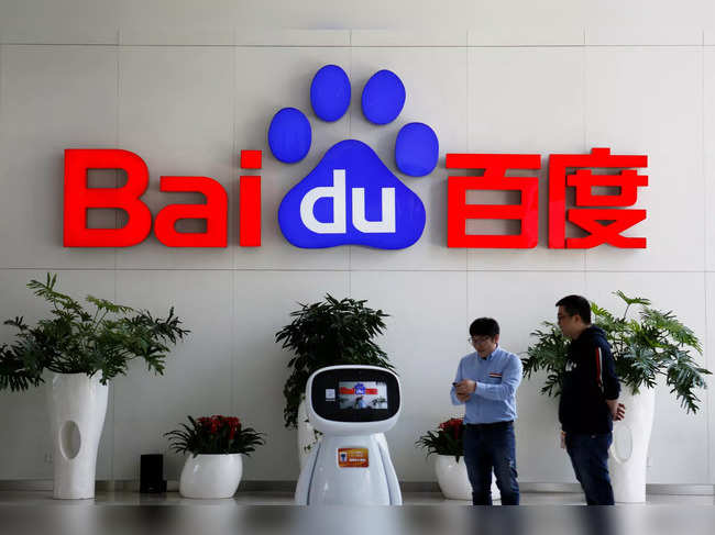 Men interact with a Baidu AI robot near the company logo at its headquarters in Beijing
