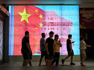 People walk past a screen showing a Chinese national flag at a shopping mall in Beijing on May 26, 2023. (Photo by Jade Gao / AFP)