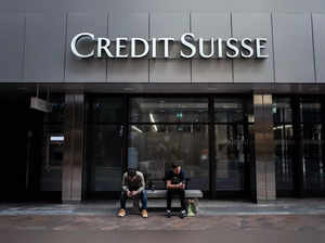 Two men sit under a sign of Credit Suisse displayed on a building in Lugano, on June 9, 2023. UBS is set to finalise the takeover of Credit Suisse on June 12, 2023, but the hardest part is yet to come: turning the arranged marriage of Switzerland's biggest banks into a success. (Photo by Fabrice COFFRINI / AFP)
