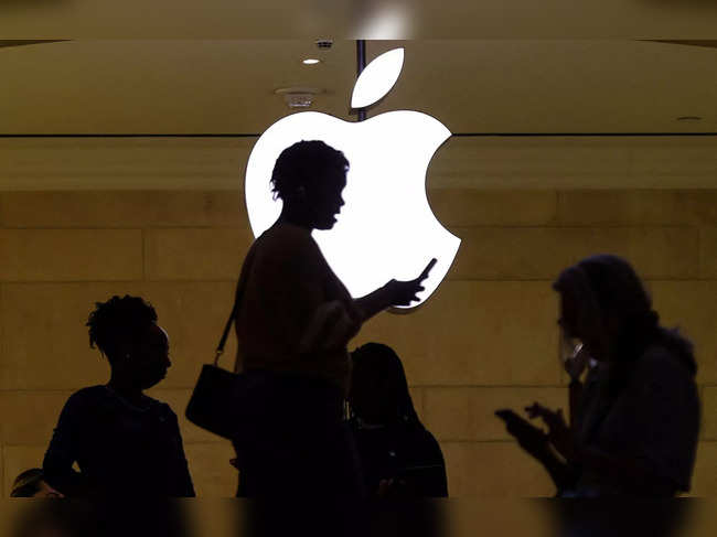 FILE PHOTO: women uses her iPhone mobile device as she passes a lighted Apple logo at the Apple store in New York