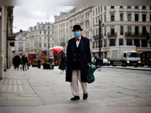(FILES) A pedestrian wearing a bow ties and bowler hat along with a face mask or covering due to the COVID-19 pandemic, walks along a quiet shopping street in central London on December 22, 2020. An enquiry probing the UK government's handling of the coronavirus pandemic kicks off Tuesday with the investigation mired in controversy even before the first witness is called. The UK suffered one of the worst Covid-19 death tolls in Europe with over 128,500 deaths recorded by mid-July 2021. (Photo by Tolga Akmen / AFP)