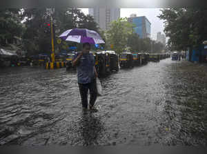 Mumbai: A commuter wades through a waterlogged road amid rain in Mumbai. (PTI Ph...