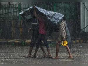 New Delhi: Pedestrians use a plastic sheet to cover themselves during monsoon ra...