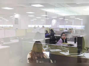 A woman is reflected on a glass as she works in a cubicle at Deloitte's office in Gurugram