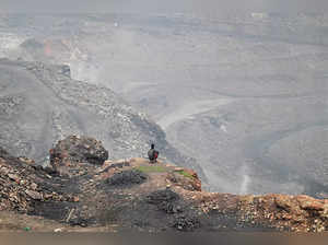 A coal picker sits near an open-cast coal mine on the outskirts of Dhanbad in India's Jharkhand state on July 6, 2023. The underground fires in open-cast coal mines in eastern India have raged for over a century, blighting the lives of millions who depend on the dirty fuel for their livelihoods. (Photo by Money SHARMA / AFP)
