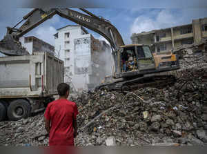 A construction worker sprays water as diggers remove the rubble of collapsed buildings, five months after a 7.8-magnitude jolt and its aftershocks wiped out swathes of Turkey's mountainous southeast, in Samandag on July 9, 2023. The excavator tore into the remnants of the damaged building in southeast Turkey, bringing them crashing down into a cloud of dust -- the latest menace facing survivors of the deadly February quake that ravaged the region. Extending to the horizon, a cocoon of fine grey dust envelops the city of Samandag, which was devastated by the February 6 earthquake that killed more than 55,000