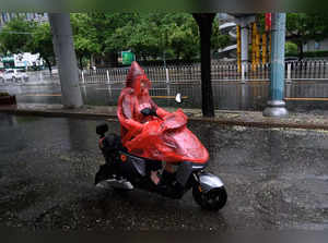 A man rides a scooter while sheltering from the rain in Beijing on July 30, 2023. China put a part of the north of the country on red alert, including the Beijing region, due to torrential rains expected from the advance of typhoon Doksuri, which is currently hitting the other end of the country. (Photo by Pedro PARDO / AFP)