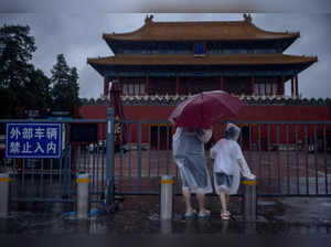 People in raincoats stand at the closed gates of the Forbidden City during heavy rain in Beijing
