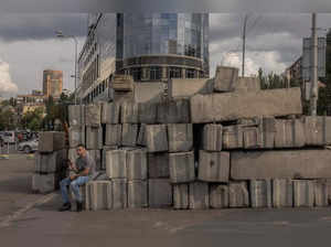 A man sits next to concrete blocks, collected from military checkpoints, in downtown Kyiv, on August 2, 2023, amid the Russian invasion of Ukraine. (Photo by Roman PILIPEY / AFP)