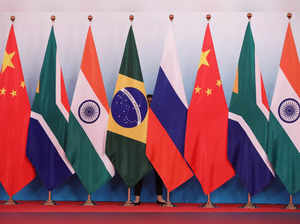 A staff worker stands behind the national flags of Brazil, Russia, China, South Africa and India to tidy the flags before a group photo during the BRICS Summit in Xiamen