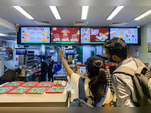 People look at the menu at a counter of a Burger King outlet in New Delhi on August 17, 2023. Soaring vegetable prices after a bad harvest have prompted Burger King's Indian outlets to take tomatoes off their menu items, following in the footsteps of other fast food giants. (Photo by Arun SANKAR / AFP)