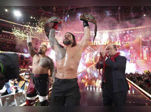 In this photo provided by WWE, Roman Reigns, center, holds up hi...