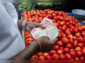 A customer counts money before paying a vegetable vendor at a market in Mumbai
