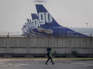 FILE PHOTO: A man carries his bag as he walks past the Go First airline, formerly known as GoAir, passenger aircrafts parked on the tarmac at the airport in New Delhi