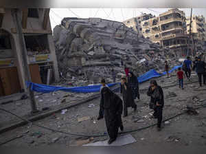 Palestinians walk by the rubble of a building after it was struck by an Israeli ...