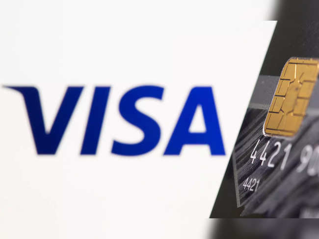 Credit card is seen in front of displayed Visa logo in this illustration