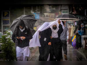 Srinagar: Students protect themselves with a scarf and umbrellas during rains, i...