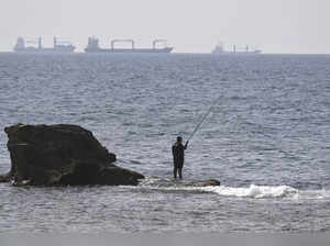 A man fishes as tankers navigate in the Mediterranean Sea off the shores of the northwestern port city of Acre on October 22, 2023, amid the ongoing battles between Israel and the Palestinian group Hamas.