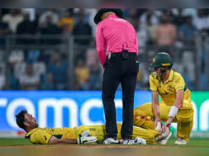 Australia's Glenn Maxwell (bottom) is being helped by his captain Pat Cummins (R) during the 2023 ICC Men's Cricket World Cup one-day international (ODI) match between Australia and Afghanistan at the Wankhede Stadium in Mumbai on November 7, 2023.