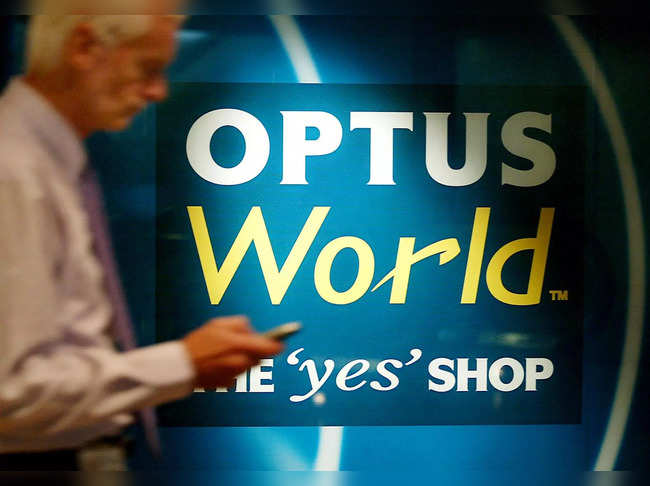 A man checks his mobile phone as he walks past an Optus sign in Sydney on May 9, 2002.