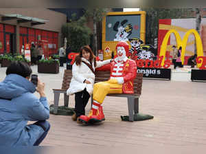 A woman sitting next to a statue of ''Ronald McDonald", the McDonald's company mascot, poses for pictures outside the McDonald's themed exhibition in Beijing