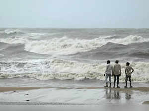 Men stand ashore while waves lash over the Kovalam beach as cyclone Michaung is expected to make landfall, in Chennai on December 3, 2023.