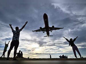 This photograph taken on November 18, 2023, shows tourists posing for pictures on the Mai Khao Beach as an airplane prepares to land at Phuket International Airport in the southern Thai island of Phuket.