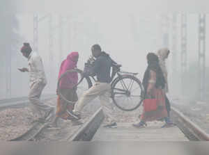 Gurugram, Dec 23 (ANI): Commuters cross a railway track amid a foggy winter morn...