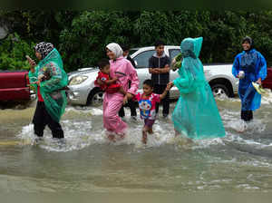 Women wear rain ponchos as they walk with children through floodwaters following heavy rain in Thailand's southern province of Narathiwat on December 25, 2023.