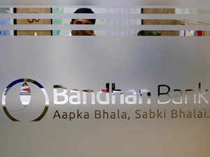An employee of Bandhan Bank is seen behind a glass bearing the bank's logo inside a branch office in Kolkata