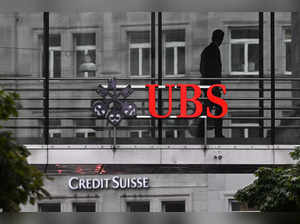 An employee of multinational investment bank UBS walks past a sign of Swiss giant banking UBS above a sign of Credit Suisse in Zurich on August 30, 2023 on the eve of the of the announcement of its first results since Credit Suisse merger.