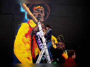 FILE PHOTO: A woman paints graffiti of the rock star Jimi Hendrix, on the wall of a music shop in Malaga