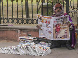 New Delhi: A vendor reads a newspaper as he waits for the customers, in New Delh...