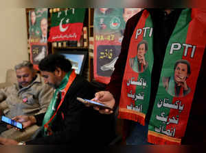 Pakistan's former prime minister Imran Khan's supporters wear scarves with prints of his Pakistan Tehreek-e-Insaf (PTI) party as they listen to a virtual election campaign on phones at Khan's PTI office in Islamabad on February 3, 2024.