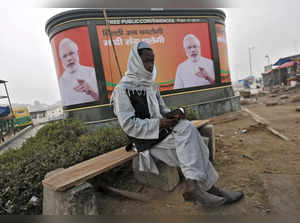 A Muslim man reads the Koran as he sits in front of a billboard featuring India's Prime Minister Narendra Modi on a pavement along a road in New Delhi