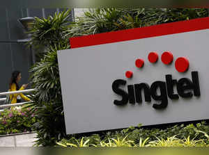 FILE PHOTO: A woman using a mobile phone walks behind a Singtel signage at their head office in Singapore