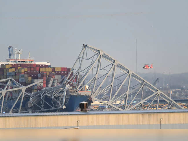 The steel frame of the Francis Scott Key Bridge sits on top of a container ship as a helicopter makes a pass after the bridge collapsed in Baltimore, Maryland, on March 26, 2024.