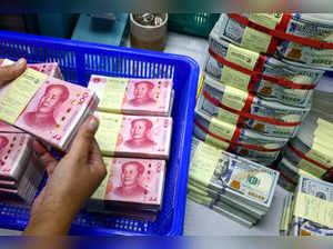 FILE PHOTO: A bank employee counts China’s renminbi (RMB) or yuan notes next to U.S. dollar notes at a Kasikornbank in Bangkok