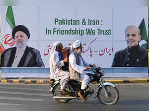 Commuters ride past a welcoming billboard displaying images of the Iranian president Ebrahim Raisi and Pakistan's Prime Minister Shehbaz Sharif, along a street in Lahore on April 22, 2024.