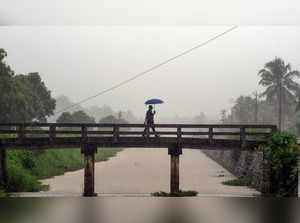 Thiruvananthapuram: A man holding an umbrella walks on a bridge during a rain on...