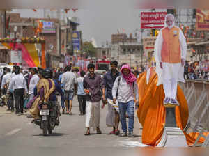 Ayodhya: People walk past a cutout of Prime Minister Narendra Modi on a hot summ...
