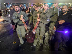 Israeli police detain a protester during a demonstration by relatives and supporters of Israelis taken hostage by Palestinian militants in Gaza in the October 7 attacks shield themselves from a police water cannon, calling for their release in the central city of Tel Aviv on May 26, 2024, amid the ongoing conflict in the Gaza Strip between Israel and the Palestinian militant Hamas group.