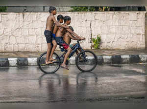 New Delhi: Children ride a bicycle during a brief spell of rain on a hot summer ...