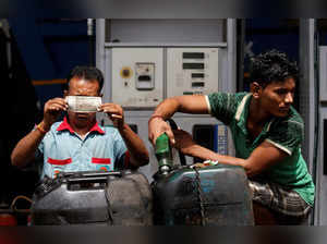 A worker checks a 500 Indian rupee note as a man fills diesel in containers at a fuel station in Kolkata