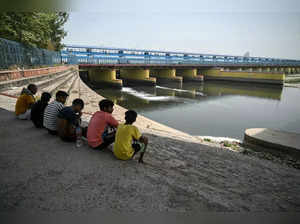 Children sit near the Yamuna river as its water level dip in, during a hot summer day in New Delhi