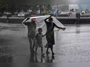 Solapur: A woman covers herself and her children with a plastic sheet as it rain...