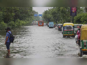New Delhi: Commuters wade through a waterlogged street after rains, in New Delhi...