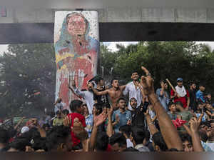 Protesters celebrate beside a defaced portrait of Prime Minister Sheikh Hasina a...